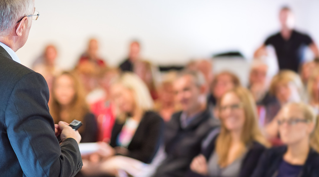 Image of speaker at a conference with people in audience