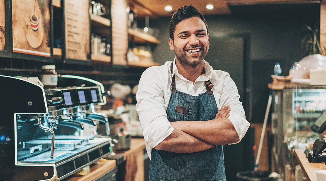 Coffee shop worker is standing in front of machine smiling