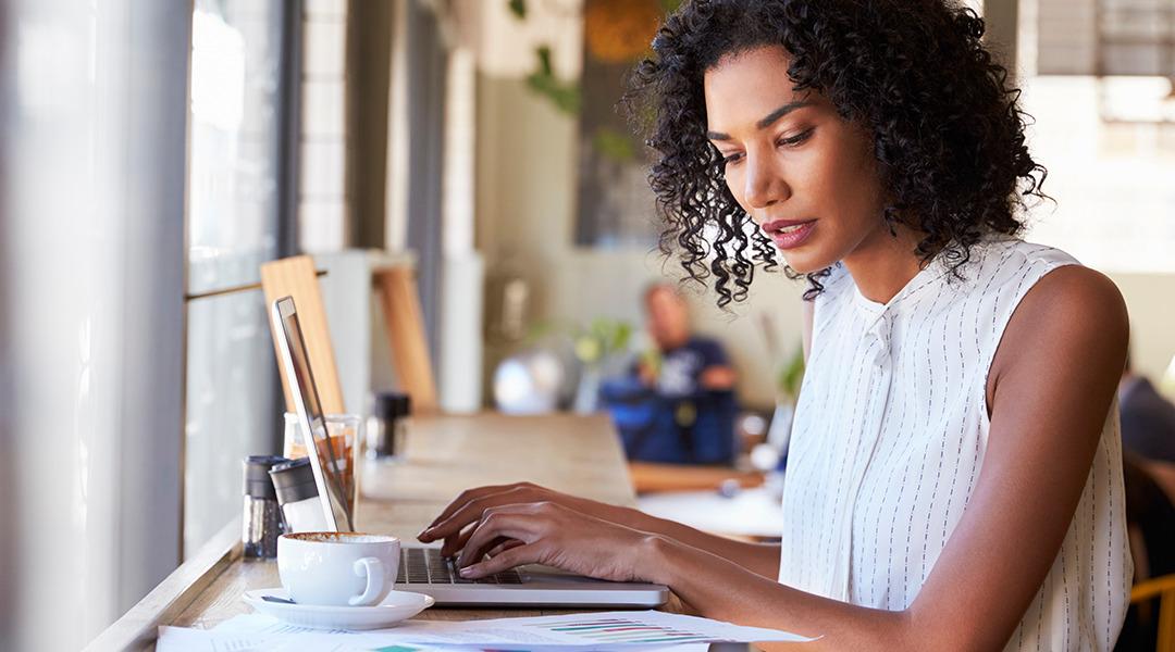 Woman in coffee shop working on laptop looking at papers