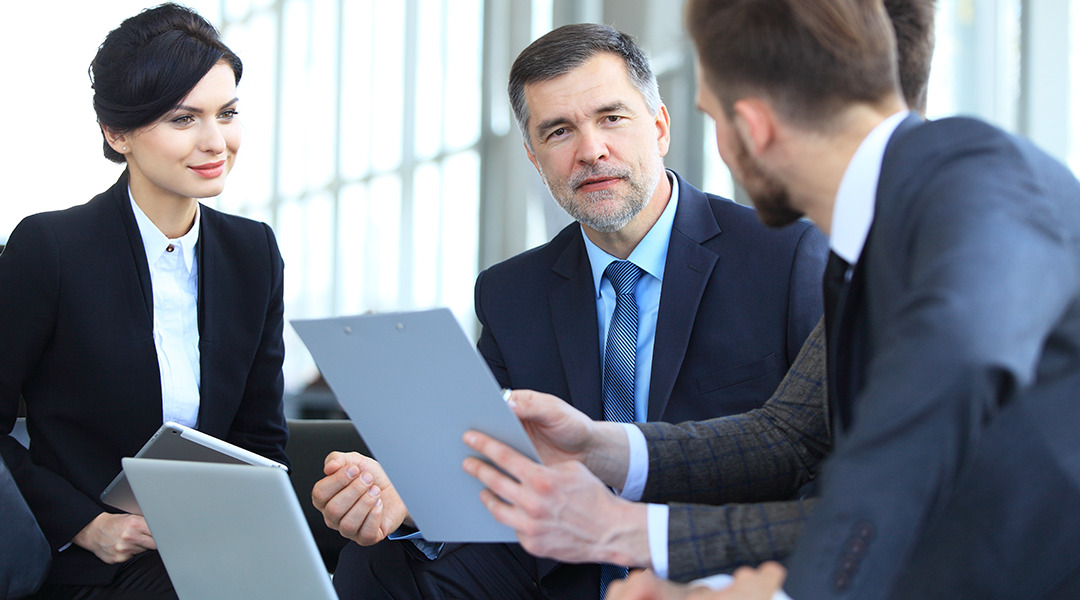 Four people in suits sit in meeting and discuss options