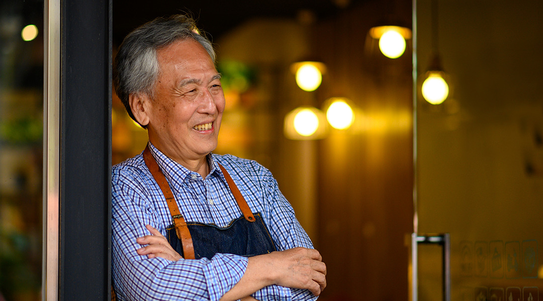 Smiling older man in apron leans against door of a store