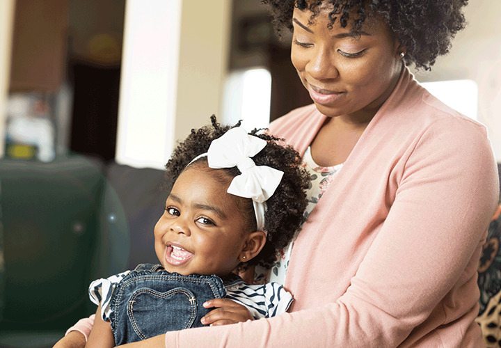 Woman holding her smiling child looks down and smiles