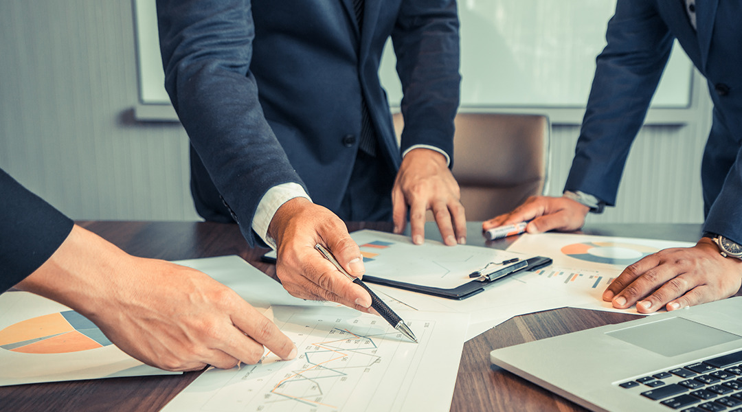 Several business people stand around table reviewing papers