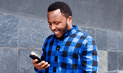 Walking man smiles and looks down at his phone in left hand