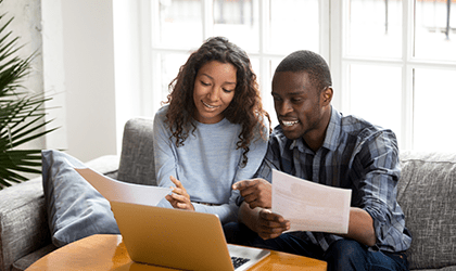 Couple seated on couch look at laptop on coffee table