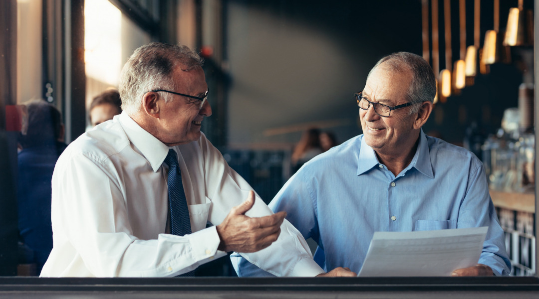 Two men are sitting in a coffee shop discussing paperwork