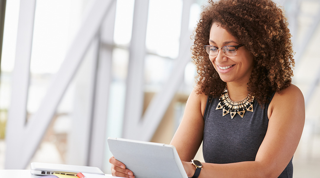 Woman seated at desk is looking at tablet in office