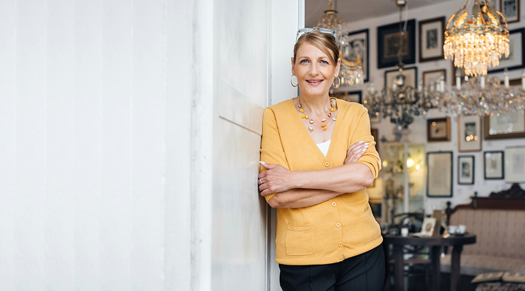 Smiling woman with glasses on her head leaning on wall