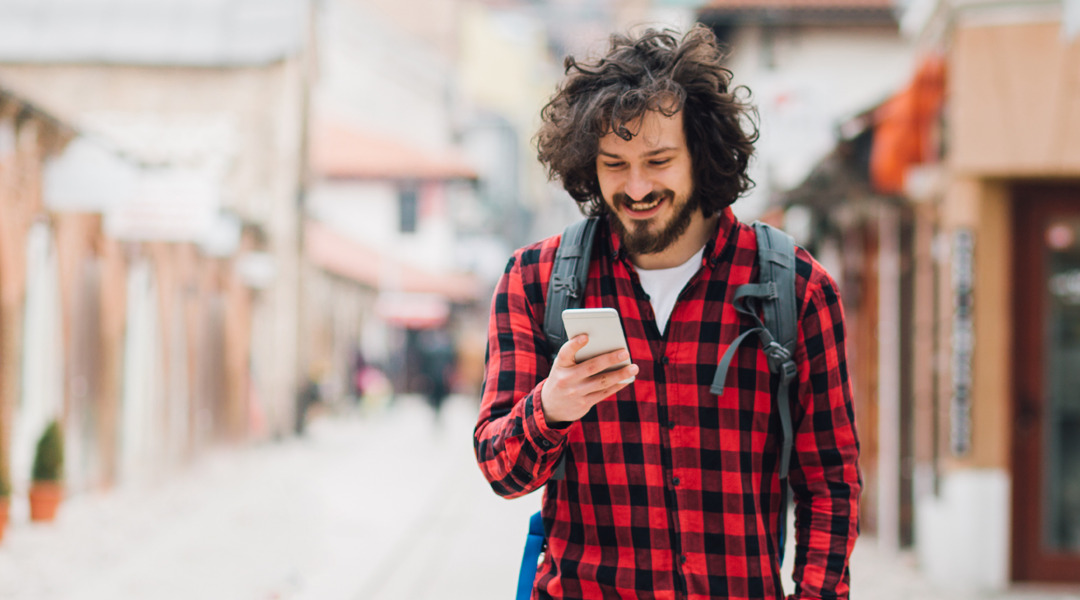 Man looks at phone and smiles while walking down street