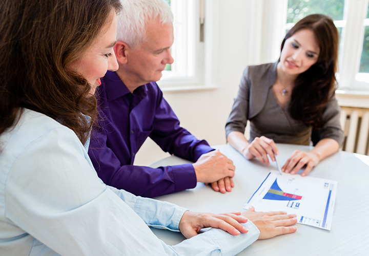 Woman reviews chart on paper with couple at a desk