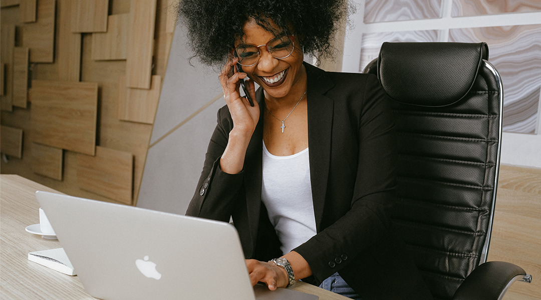 Happy woman seated looking at laptop talking on phone