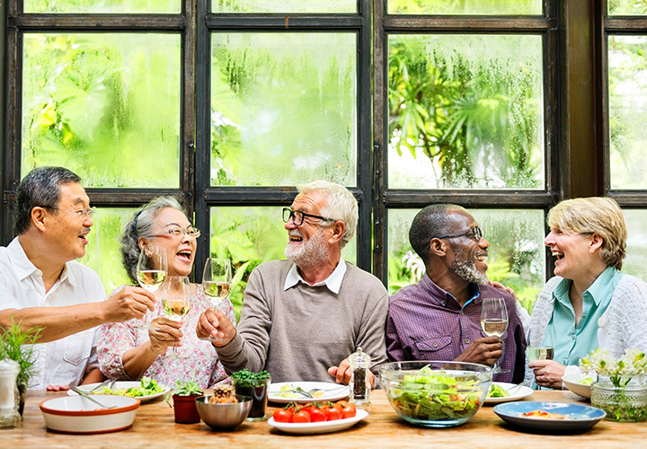 Older adults at a table share laughs with wine and food