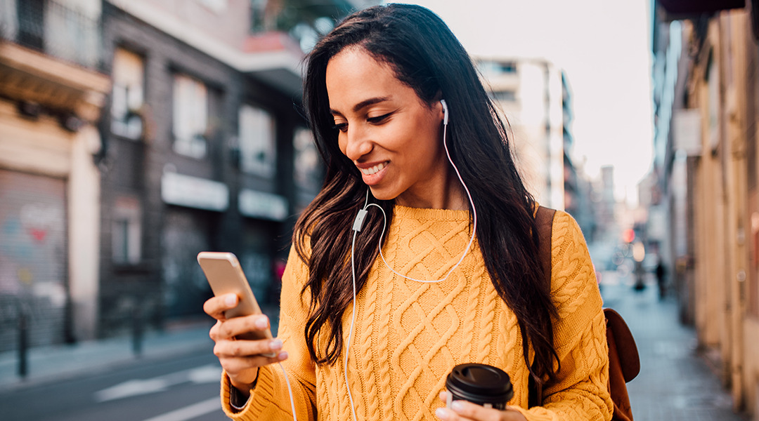 Woman on city street looking at phone holding coffee