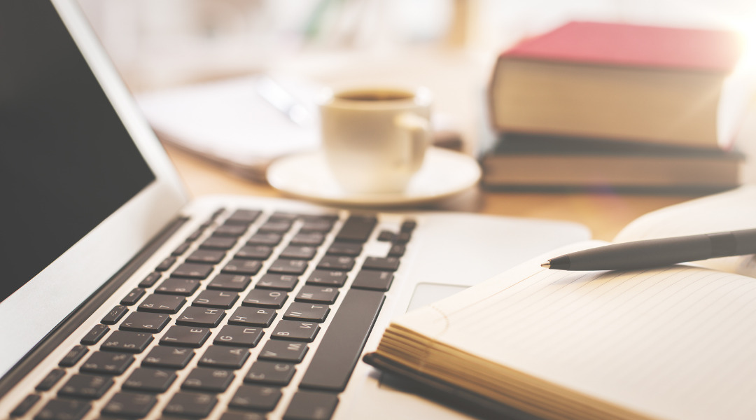 Open laptop on a table with a notebook and pen