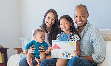 Smiling family seated on couch with child holding drawing