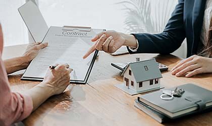 One person pointing at contract another person is signing it