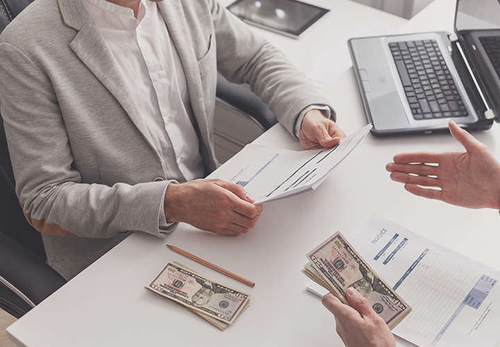 Two people seated at desk with invoices and cash on desk