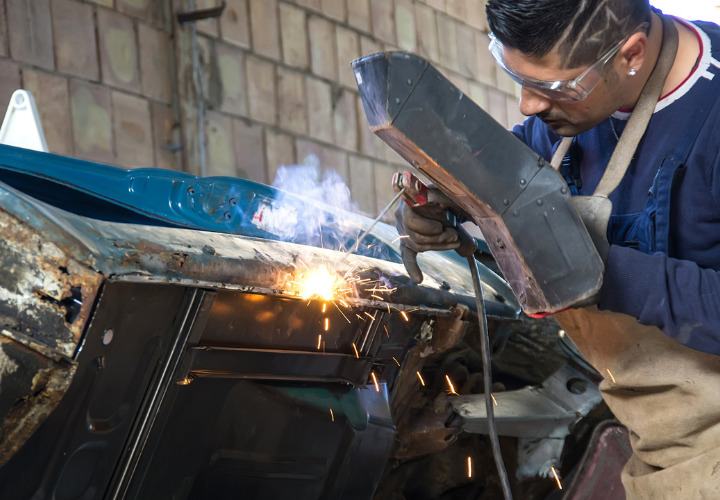 Man is repairing the side of an old car by welding