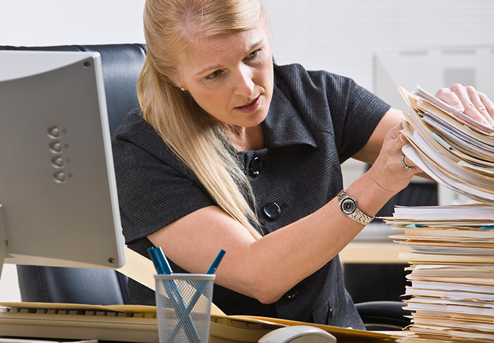 Woman at desk looking through huge stack of paperwork