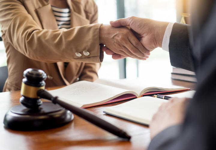 Two people shaking hands with a gavel on desk