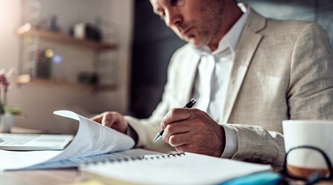 A man at desk reviewing paperwork with a pen