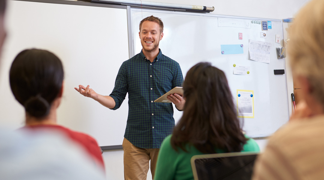 Teacher in front of class with whiteboard behind them.