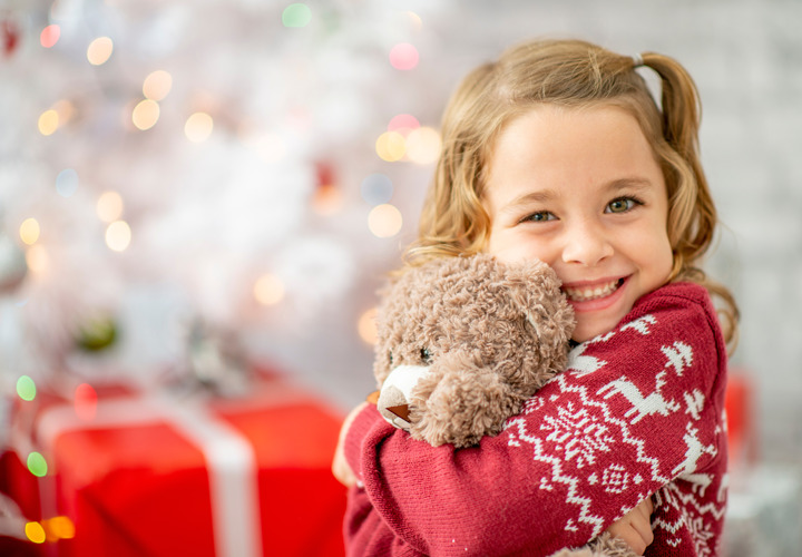 A smiling young girl holds a teddy bear in front of presents.