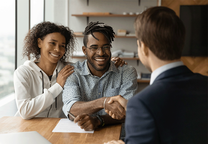 Happy people sign paperwork and shake hands with their mortgage loan officer.