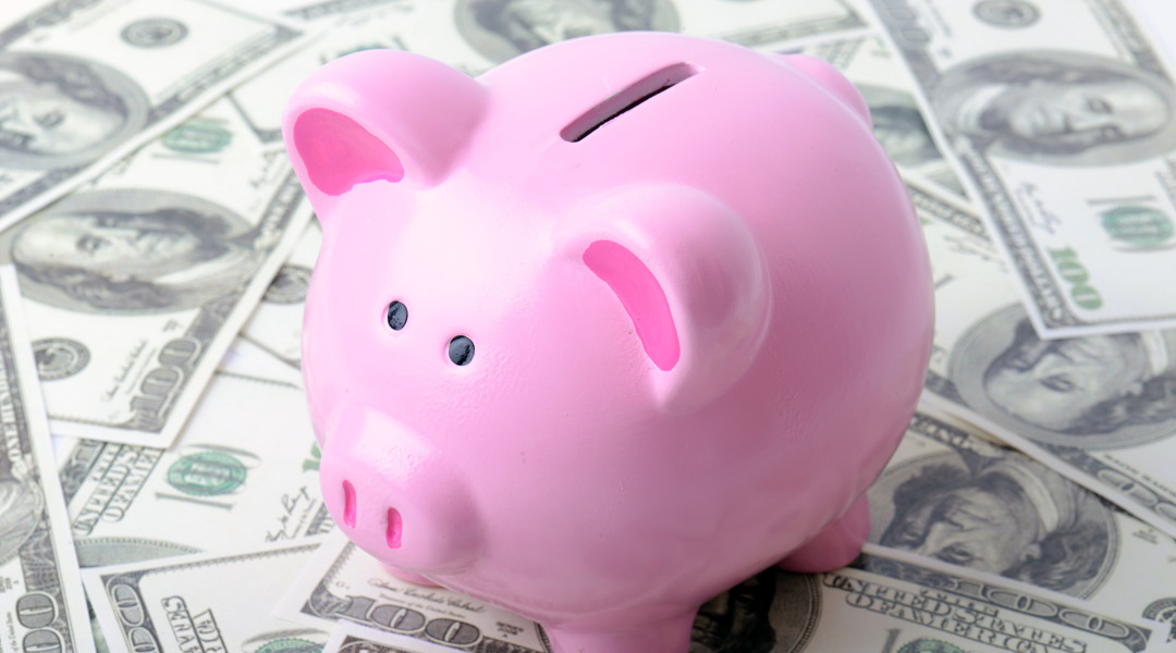 A classic pink piggy bank with 100 dollar bills spread over surface.