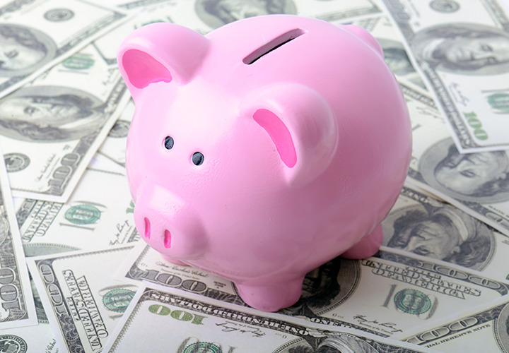 A classic pink piggy bank with 100 dollar bills spread over surface.