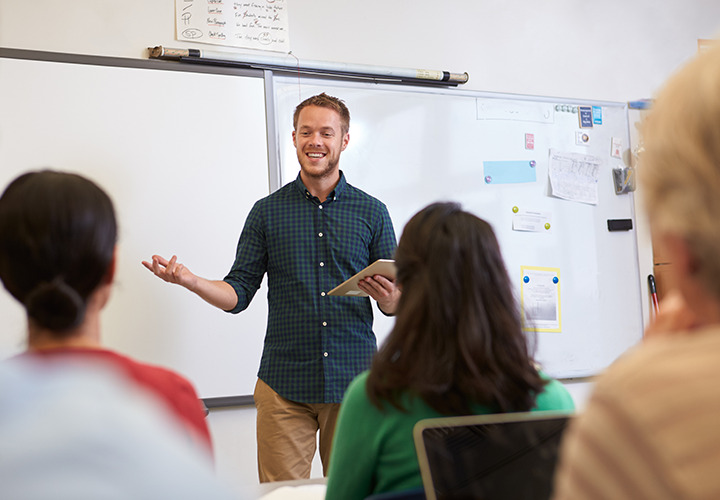 Teacher in front of class with whiteboard behind them.